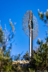 Looking rather like a toilet brush, but glistening in the sunshine is `Resilience` by Kark Meyer. A sign indicates that it represents the `heart of the community`. [4409]