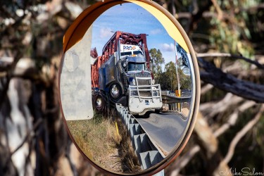 A passing truck caught in the roadside mirror — a fleeting echo of motion beside the stillness of the river. [4661]