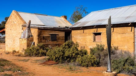 A relic turned sculpture — the propeller stands sentinel beside a weathered stone house. [3126]