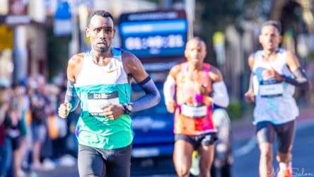 Elite runner Gobena maintains a commanding stride through Taylor Square during the 2025 Sydney Marathon. His concentration and rhythm capture the intensity of the race as the timing display looms behind him. Addisu Gobena Aga finished 2nd out of 20,824. [5358]