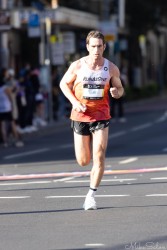 Australian runner Fraser Darcy maintains a strong pace through Taylor Square during the 2025 Sydney Marathon. Representing RunAsOne, he finished 19th out of 21,413 participants, embodying the grit and precision of elite distance running. [5383]