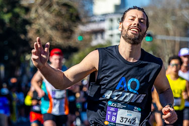 At the 32 km mark, a runner flashes a weary grin and raises his hand as if to say, “Only ten to go.” The sunlight and his relaxed stride hint at the satisfaction of endurance meeting resolve. [3990]