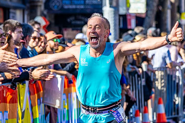 A runner reaches Taylor Square with arms outstretched, high‑fiving spectators as he soaks in the cheers. His expression says it all — the pure exhilaration of achievement and connection. [3981]